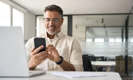 Smiling man looking at phone in front of laptop